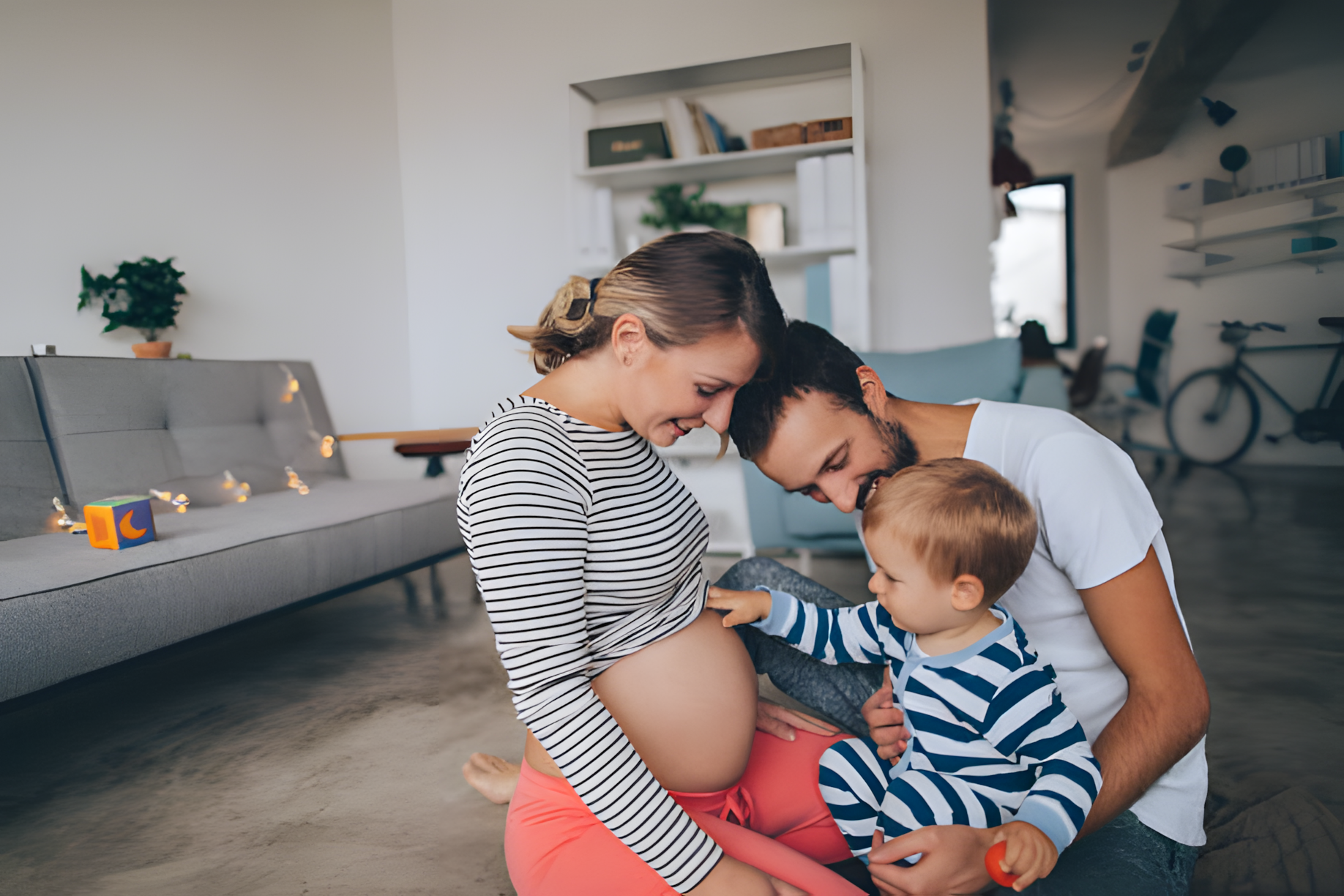 Famille souriante avec une femme enceinte, son partenaire et leur enfant, partageant un moment intime de connexion en préparation de la naissance.