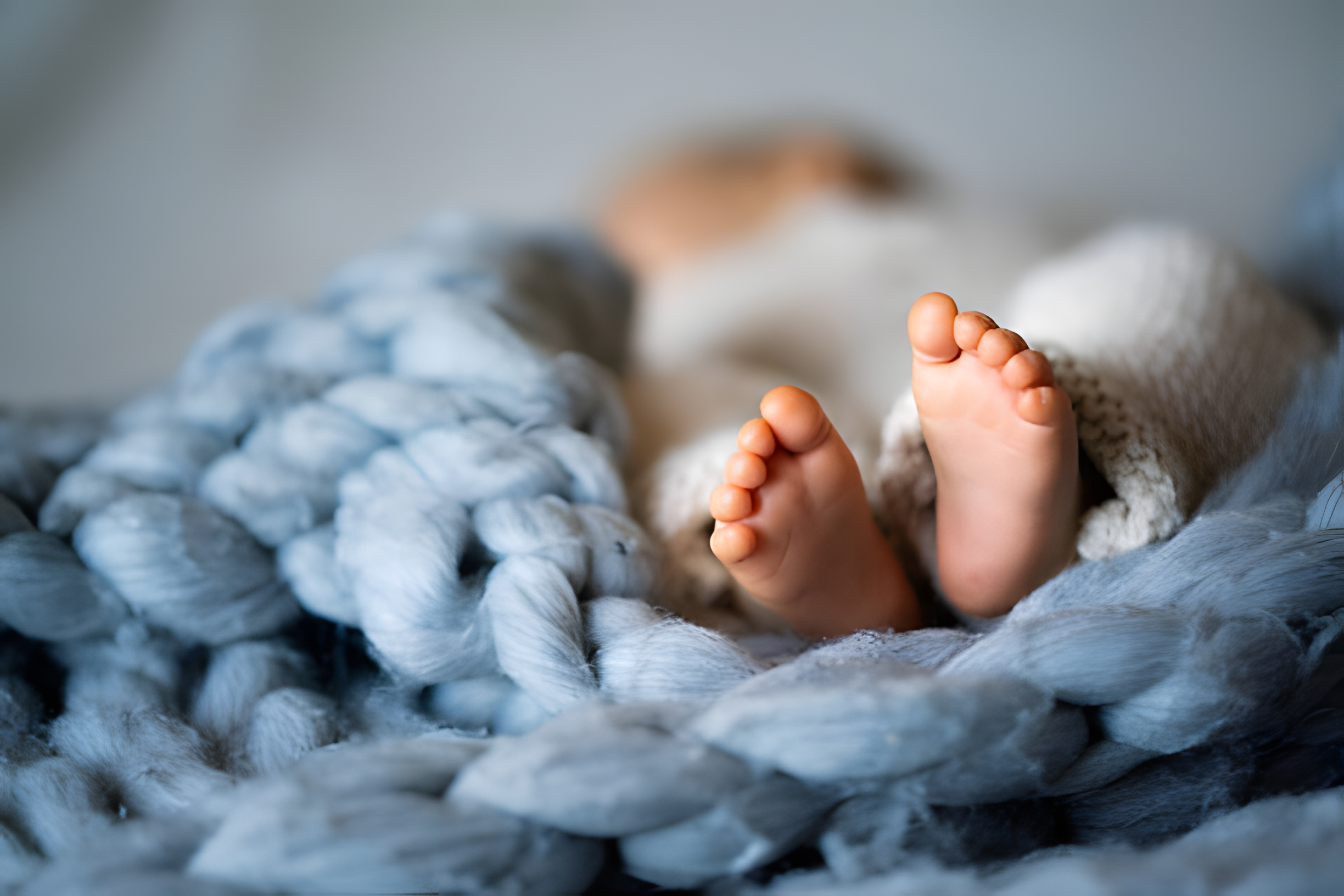 Pieds d'un nouveau-né enveloppés dans une couverture douce et moelleuse, symbolisant la présence rassurante de la doula à la naissance.